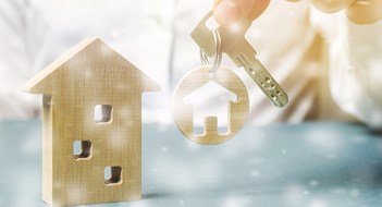 Sell the Halls (and the Bedrooms, and the Kitchen...) Trinket with miniature home in the hands of a businessman and a wooden house with snow. Christmas Sale of Real Estate. New Year discounts for buying housing. Purchase apartments at a low price.