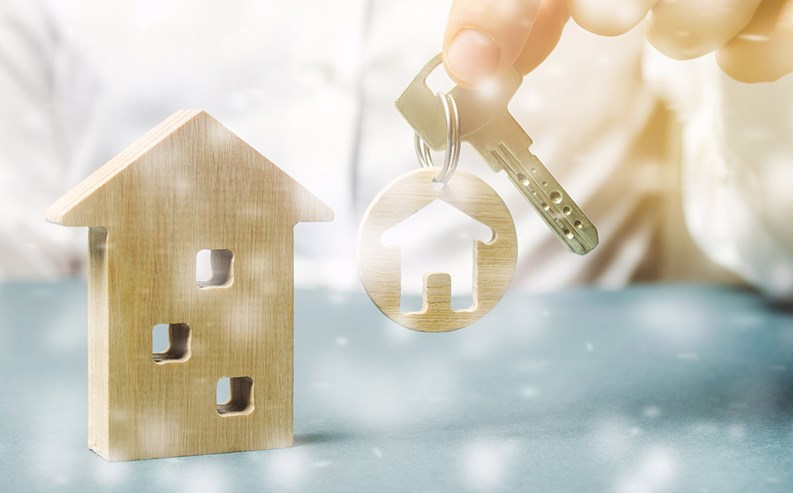 Trinket with miniature home in the hands of a businessman and a wooden house with snow. Christmas Sale of Real Estate. New Year discounts for buying housing. Purchase apartments at a low price.