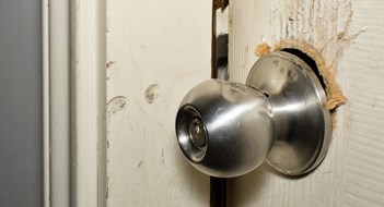 Broken modern doorknob closeup with signs of forced entry, criminal activity and door slightly open.