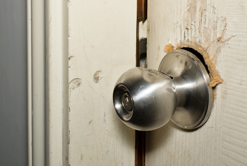 Broken modern doorknob closeup with signs of forced entry, criminal activity and door slightly open.