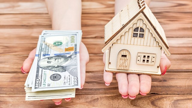 Woman's hands holding money and model of house over wooden table.