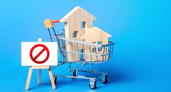 Houses in a shopping cart and easel red prohibition sign NO. Inaccessibility, lack housing, deficit. Seizure, freezing of assets by a bank, court. Expensive maintenance, impossibility of restoration