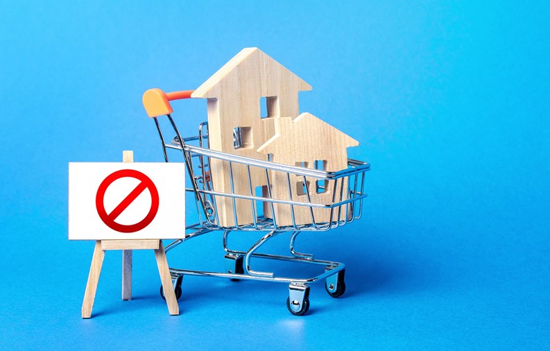 Houses in a shopping cart and easel red prohibition sign NO. Inaccessibility, lack housing, deficit. Seizure, freezing of assets by a bank, court. Expensive maintenance, impossibility of restoration