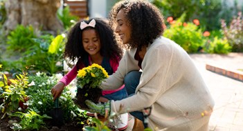The ‘3 Greens’ of Landscaping: Happy african american mother and daughter planting flowers. family time, having fun together at home and garden.