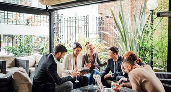 Group of business people are discussing their work in a bar courtyard after work. They are drinking cocktails and using technology.