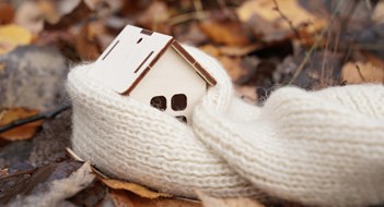 Medicine and weather concept. A wooden house wrapped in a scarf stands on fallen leaves.