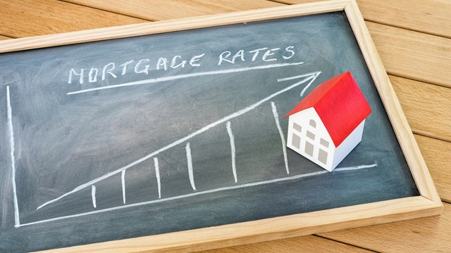 Graph representing the rise in mortgage interest rates drawn on a chalkboard lying on a wooden table. A model of a house with a red roof is on the chalkboard. Finance and real estate concept.