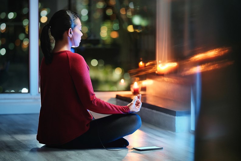 Girl doing yoga training at home at night. Young Latin American woman meditating using an app on smartphone.