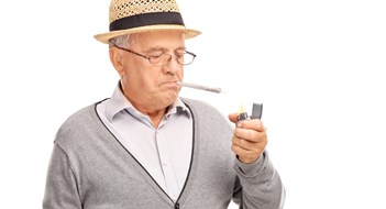 Senior man lighting up a joint with a gray lighter isolated on white background