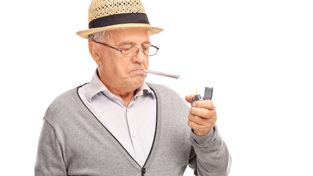 Senior man lighting up a joint with a gray lighter isolated on white background