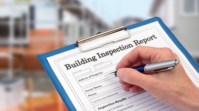 Buiding Inspector completing an inspection form on clipboard beside new build construction