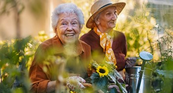 Managing Aging Residents Portrait of senior friends taking care of vegetable plants in urban garden in the city. Pensioners spending time together gardening in community garden in their apartment complex. Nursing home residents gardening outdoors. Senior sisters have same hobby.