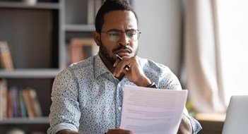 Understanding Management Fees African student guy sit at desk hold papers tasks having difficulties with test, company lawyer read contract terms and detail feels discontented, received bad news from bank unpleasant letter concept
