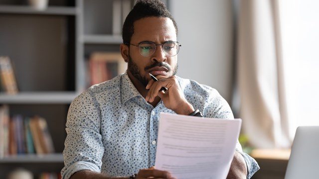 African student guy sit at desk hold papers tasks having difficulties with test, company lawyer read contract terms and detail feels discontented, received bad news from bank unpleasant letter concept