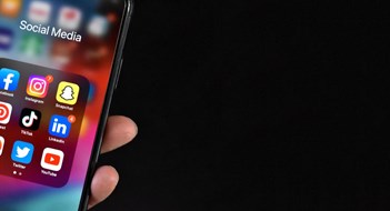 Social Media for Multifamily Communities Hand Holding Cell Phone with Social Media Apps Facebook, Instagram, SnapChat, Pinterest, TikTok, LinkedIn, Reddit, Twitter and YouTube on Device Screen, Smartphone Mobile Online Application Icons Over Black Background with Copy Space, Panoramic