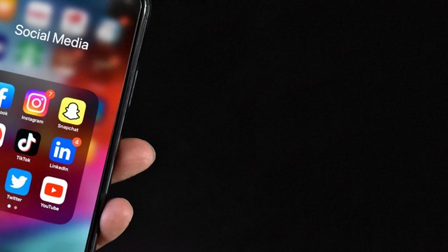 Hand Holding Cell Phone with Social Media Apps Facebook, Instagram, SnapChat, Pinterest, TikTok, LinkedIn, Reddit, Twitter and YouTube on Device Screen, Smartphone Mobile Online Application Icons Over Black Background with Copy Space, Panoramic