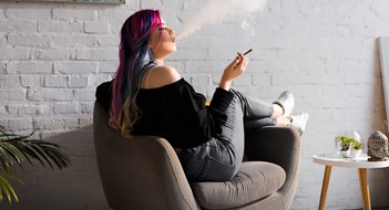 Managing Cannabis side view of hipster girl with colorful hair sitting in armchair and blowing smoke