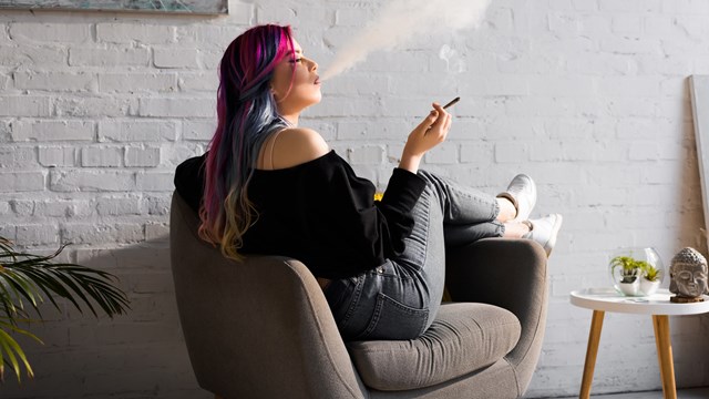 side view of hipster girl with colorful hair sitting in armchair and blowing smoke