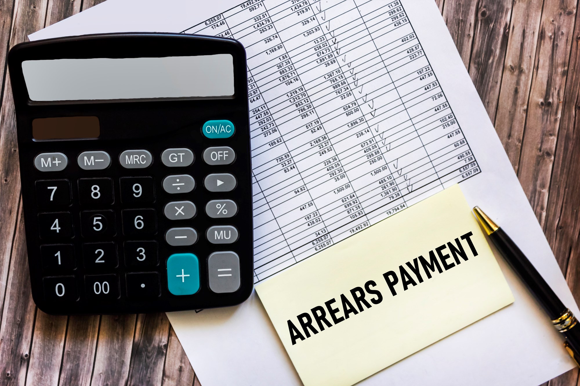 Payment arrears are written in a notepad, on a wooden table with a calculator and documents