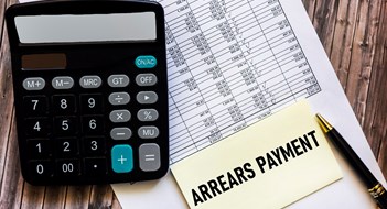 Collecting Arrears Payment arrears are written in a notepad, on a wooden table with a calculator and documents