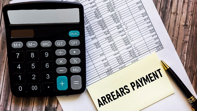 Payment arrears are written in a notepad, on a wooden table with a calculator and documents