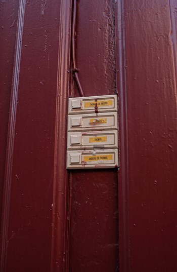 Closeup of weathered doorbell panel on red wooden wall